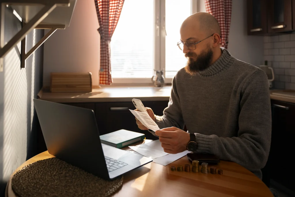 Pracownik zdalny analizujący rachunki i dokumenty przy laptopie w domowym biurze